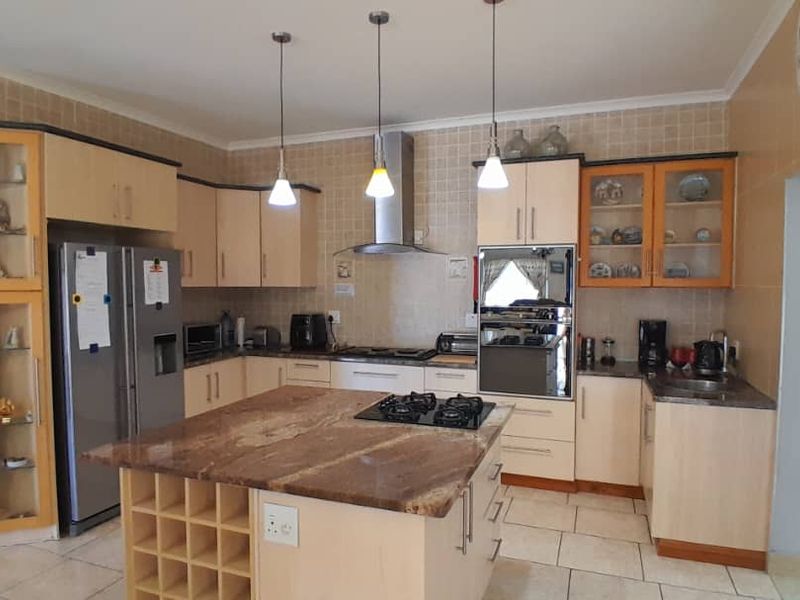 Spacious kitchen featuring light wood cabinetry, granite countertops, a central island with a gas hob, and integrated oven with extractor fan.