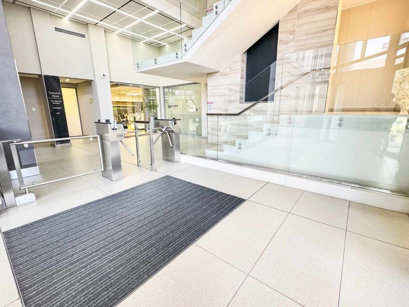Modern commercial building entrance lobby featuring secure turnstile access, glass balustrades, and high-quality tiled flooring with clear directory signage.