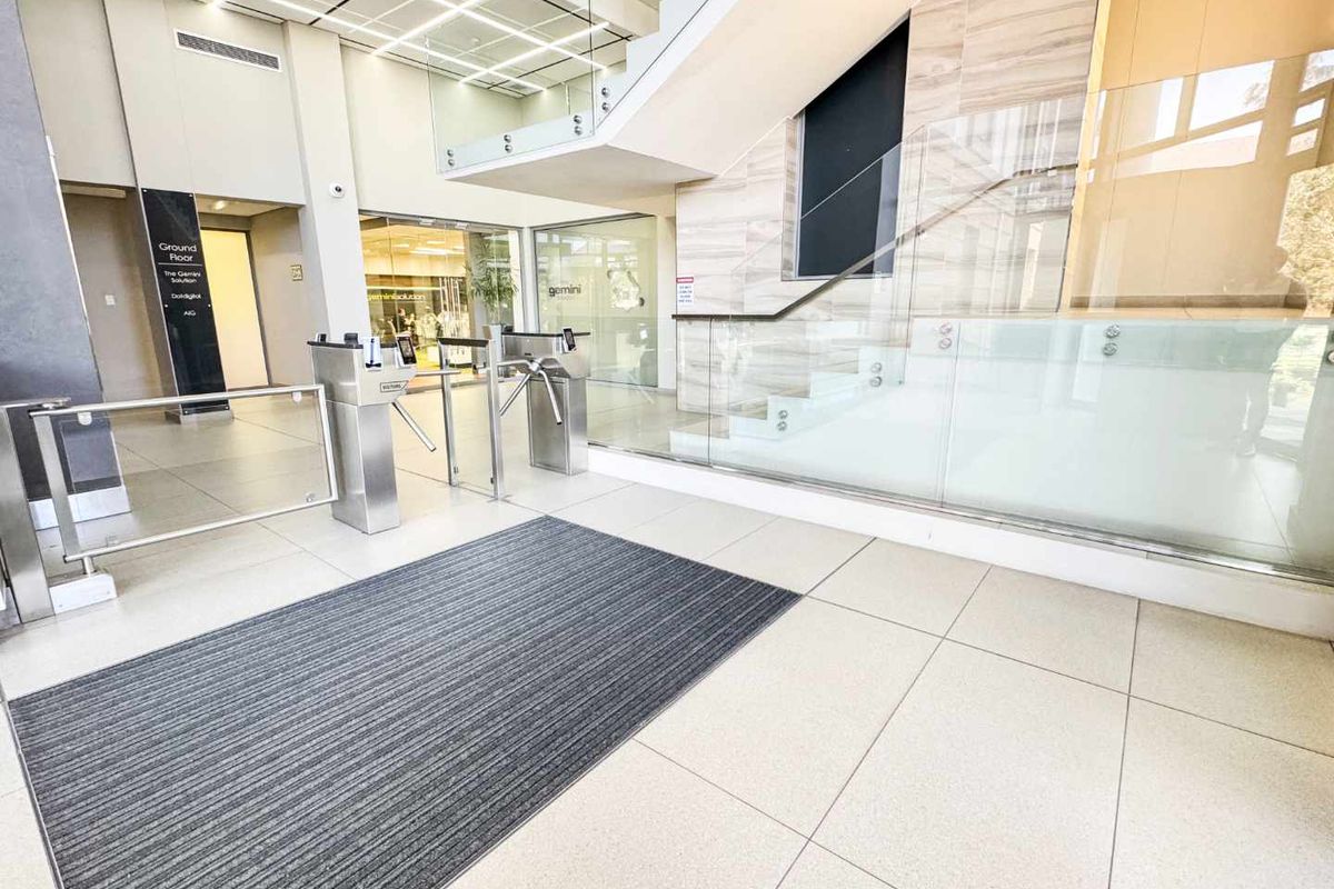 Modern commercial building entrance lobby featuring secure turnstile access, glass balustrades, and high-quality tiled flooring with clear directory signage.