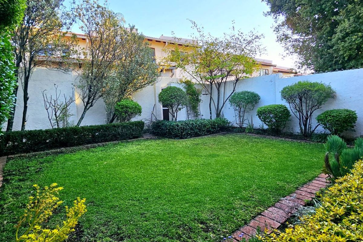 A well-maintained private rear garden featuring a lush green lawn, established shrubbery, and a secure boundary wall.