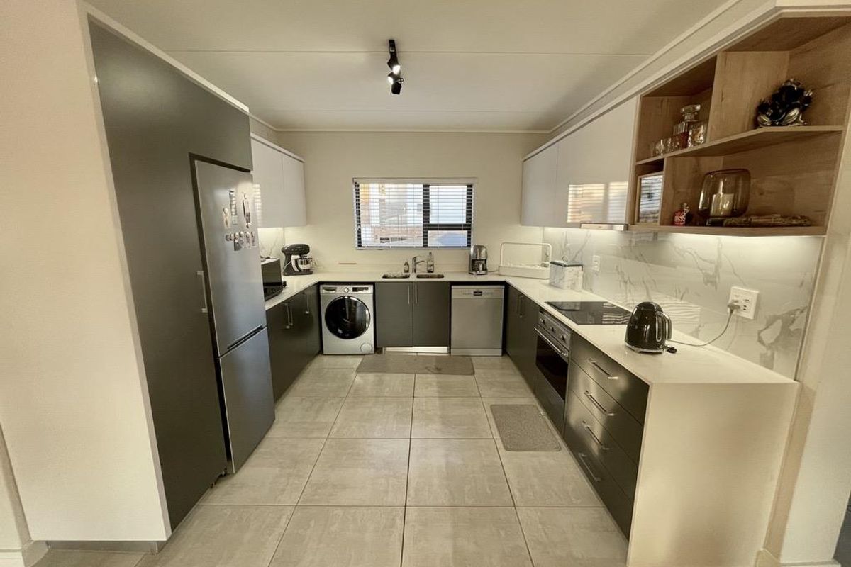 Modern U-shaped kitchen featuring sleek two-tone cabinetry, stone countertops, marble-look splashback, integrated appliances, and large format floor tiles.