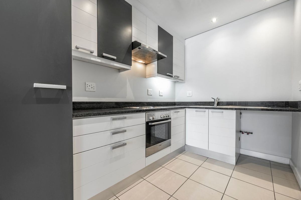 Modern kitchen featuring sleek white and dark cabinetry, granite countertops, built-in oven, extractor fan, and tiled flooring.