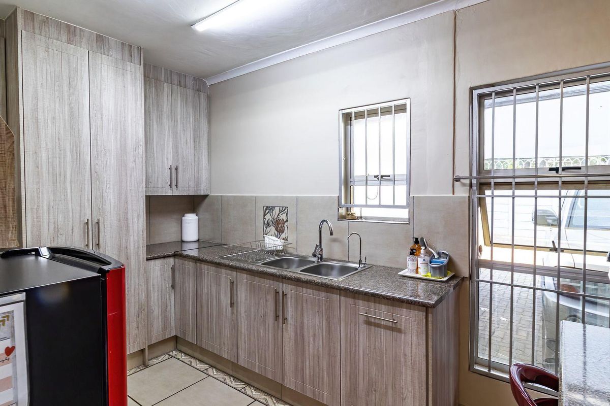 A functional office kitchenette featuring wood-grain cabinetry, granite countertops, a double stainless steel sink, and security bars on the windows.