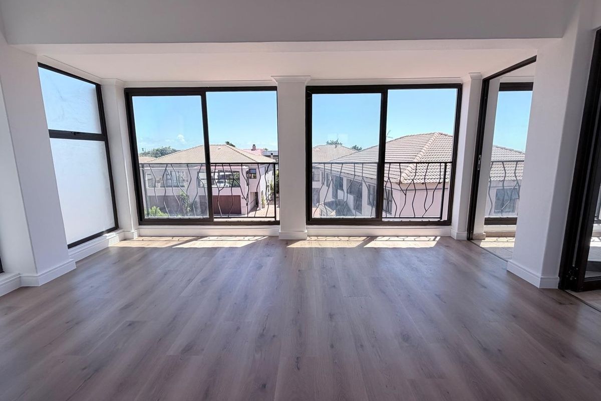 A bright, empty living area featuring modern wood-look flooring and large sliding glass doors that open onto a balcony with neighborhood views.