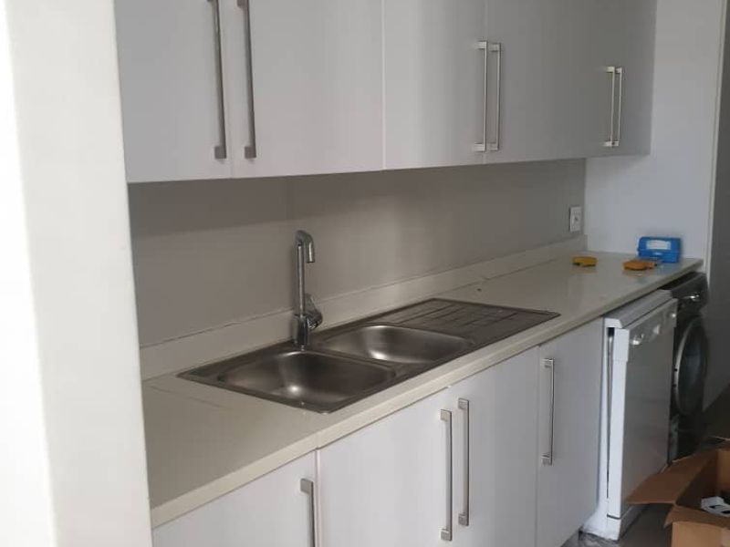 A clean, modern kitchen featuring white built-in cabinetry, stone countertops, and a stainless steel double sink with a contemporary mixer tap.