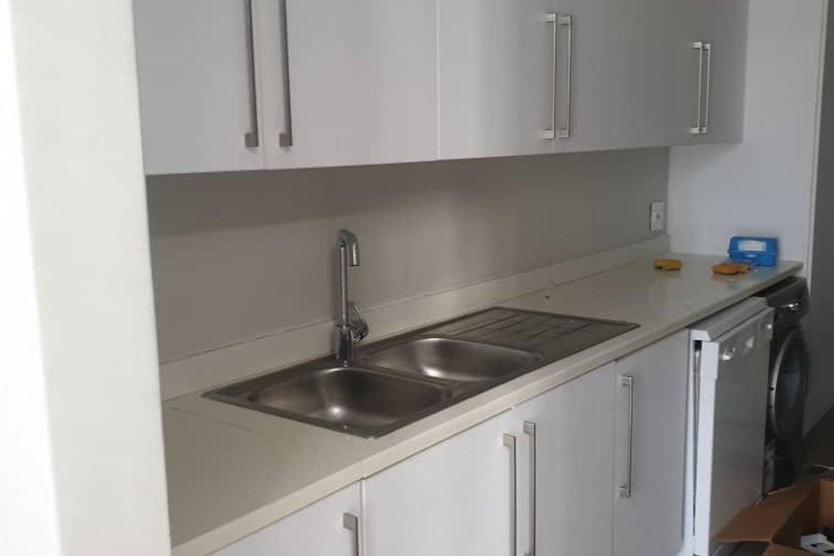A clean, modern kitchen featuring white built-in cabinetry, stone countertops, and a stainless steel double sink with a contemporary mixer tap.