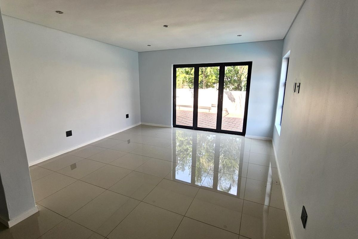 A bright, spacious living area featuring large porcelain floor tiles and black-framed sliding glass doors that open to an outdoor patio.