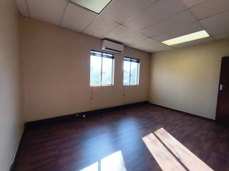 A vacant office space featuring laminate flooring, a suspended ceiling with recessed lighting, and a wall-mounted split-system air conditioning unit.