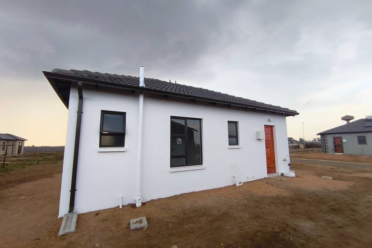 A view of the rear exterior of a modern house featuring white plastered walls, dark roof tiles, and a wooden entrance door.