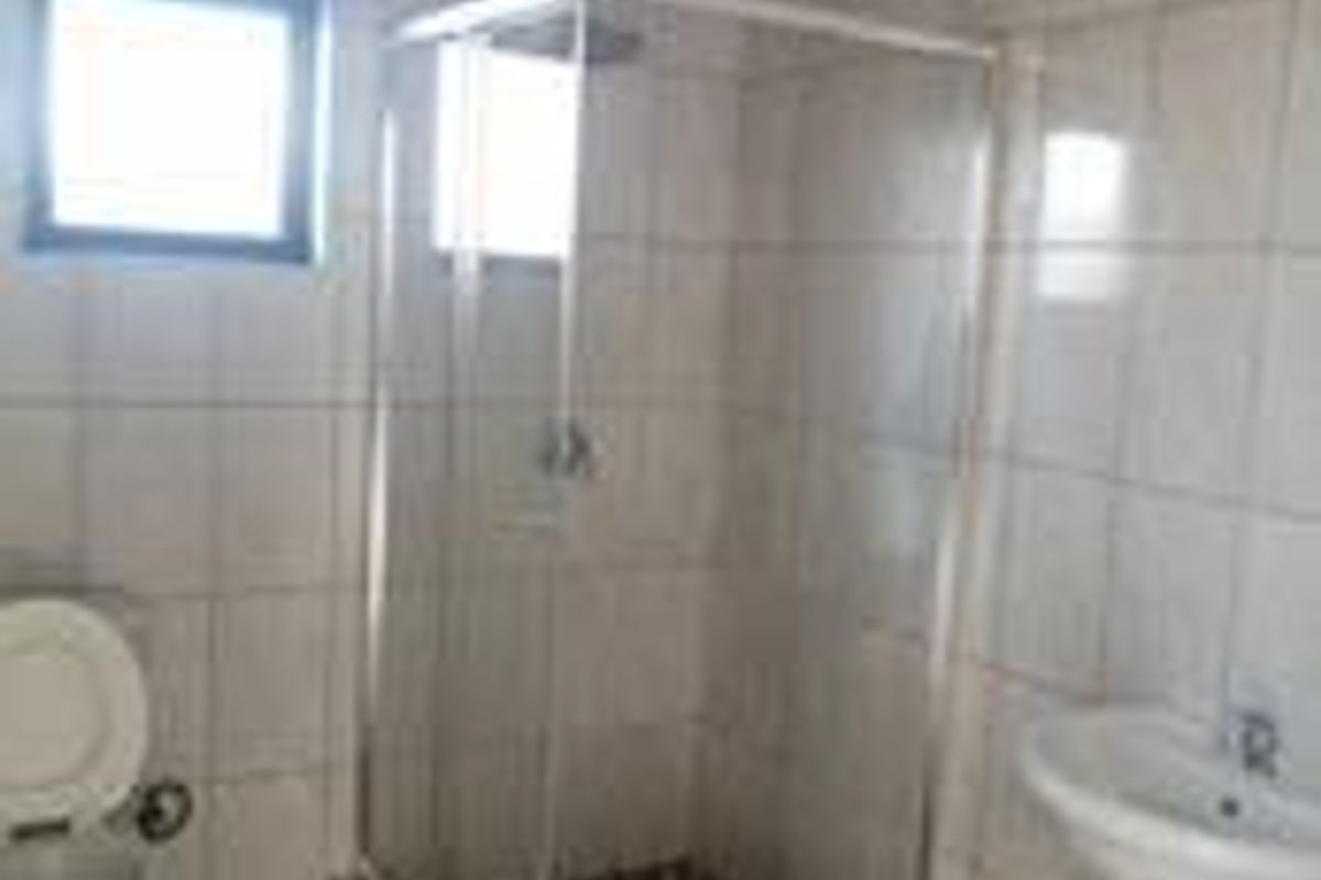 A functional bathroom featuring a glass shower enclosure, pedestal basin, and toilet with neutral wall and floor tiling.
