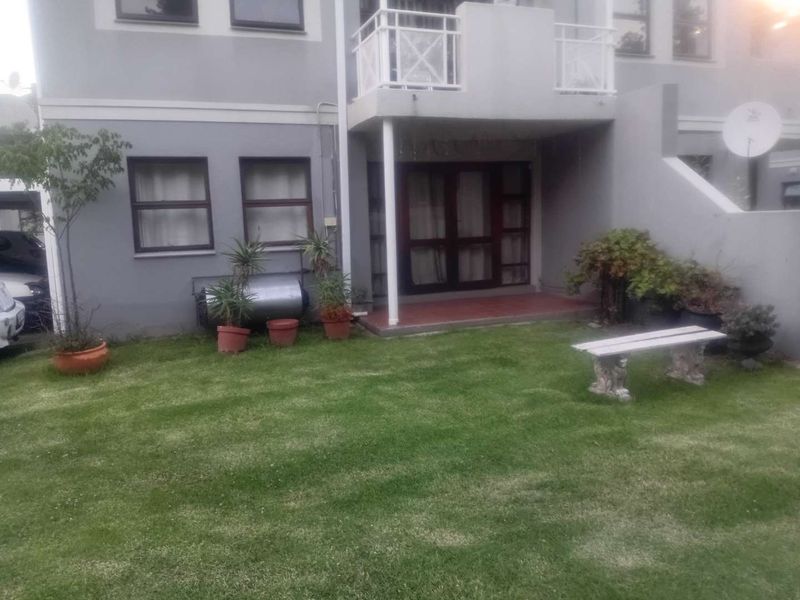 Rear view of the apartment building featuring a small lawn, a ground-level patio, and an upper-level balcony with white railings.