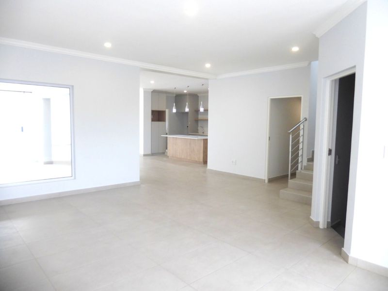 Spacious open-plan living area featuring neutral tiled flooring, recessed lighting, and a modern kitchen with a central island and staircase access.