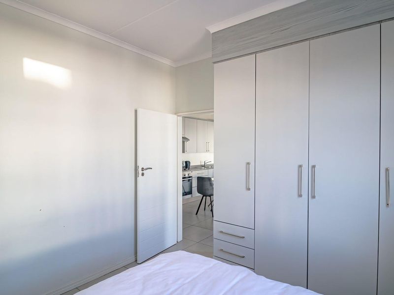 A bright bedroom featuring modern built-in cupboards with integrated drawers and neutral tiled flooring, offering a clean and functional living space.
