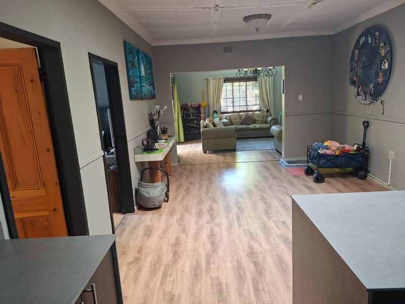 Open plan living area featuring laminate flooring and neutral wall tones, connecting to an adjacent lounge space with natural light.