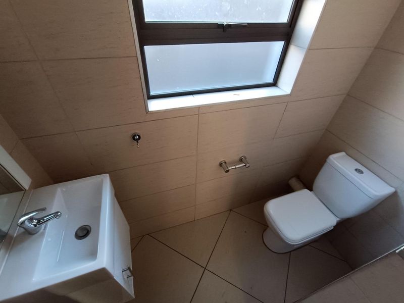 A clean and functional bathroom featuring tiled walls and flooring, a modern basin with chrome mixer, and a white toilet.