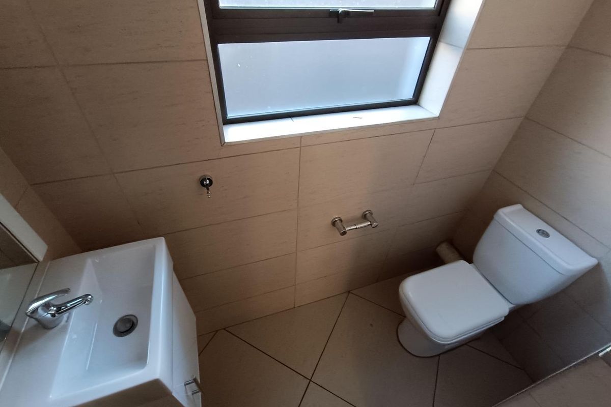 A clean and functional bathroom featuring tiled walls and flooring, a modern basin with chrome mixer, and a white toilet.