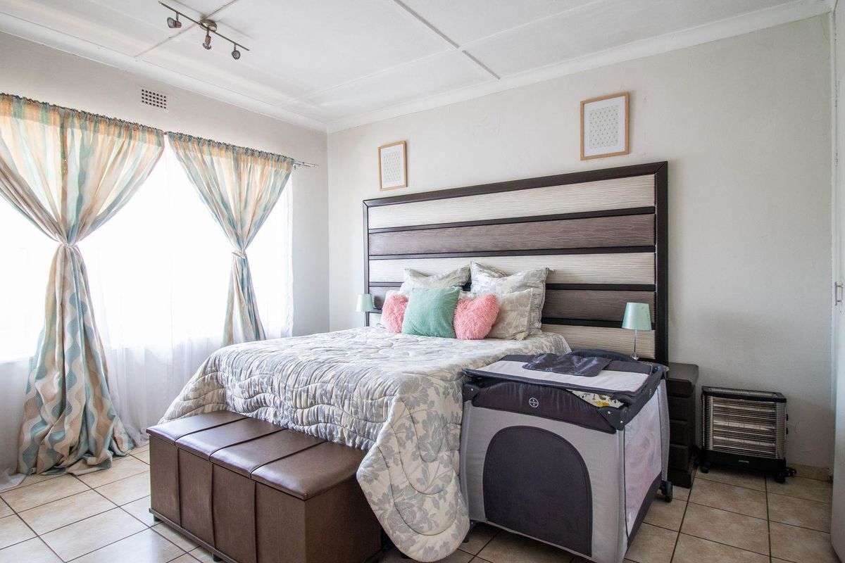 A well-lit bedroom featuring tiled flooring, a large window with curtains, and a ceiling-mounted track lighting fixture.