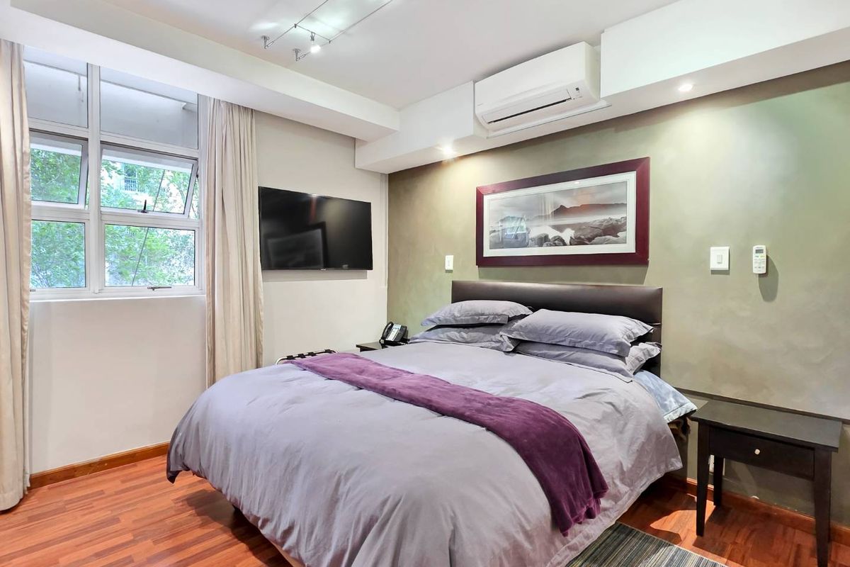 A well-maintained bedroom featuring laminate flooring, a split-system air conditioner, and modern track lighting, offering a comfortable and functional living space.