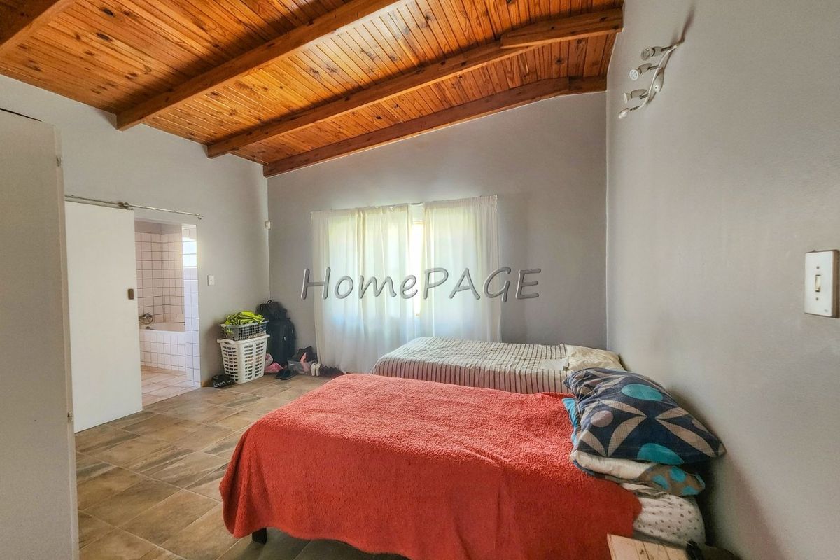 Spacious bedroom featuring exposed timber beam ceilings, tiled flooring, and direct access to an en-suite bathroom.