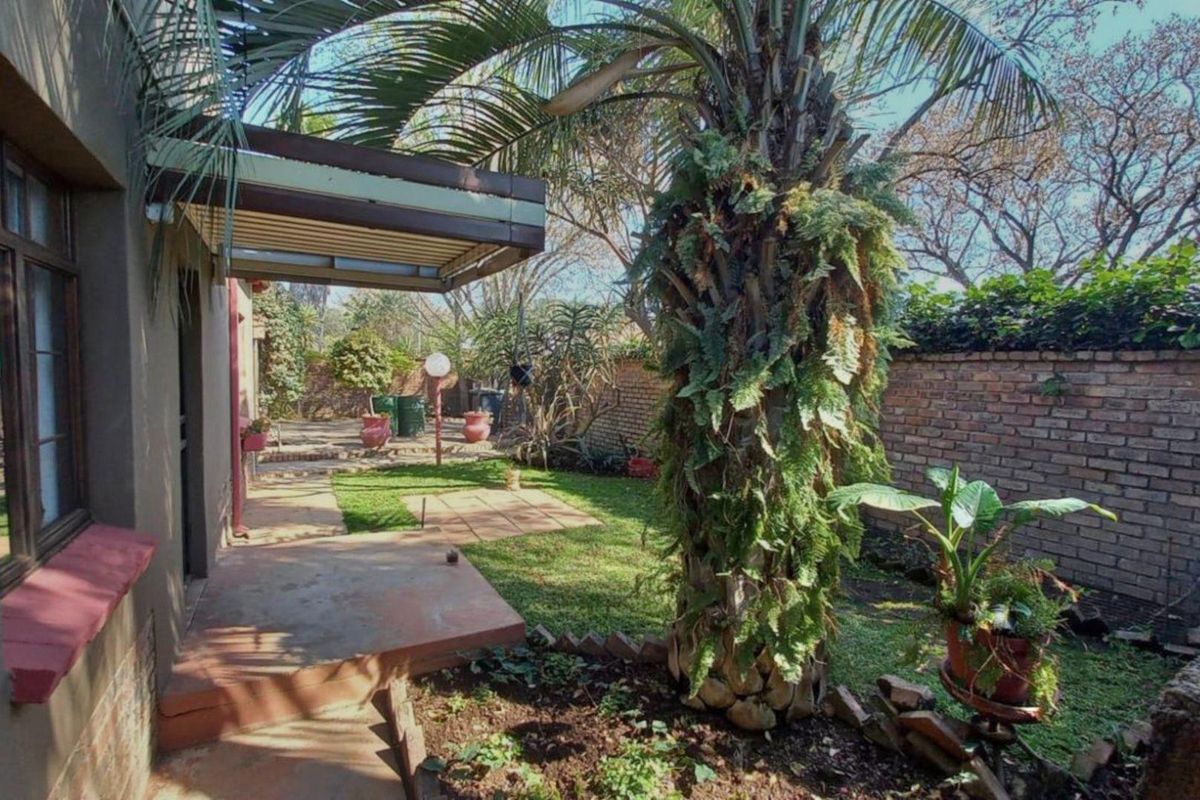 A rear garden area featuring a covered patio, paved pathways, and a brick boundary wall, providing a private outdoor space.