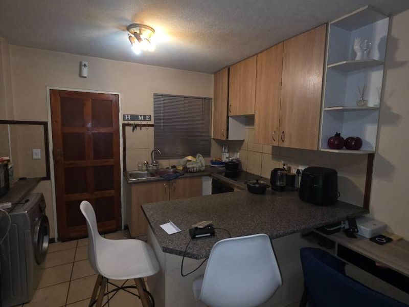 Compact kitchen featuring laminate cabinetry, a breakfast bar, tiled flooring, and a tiled backsplash, offering a functional layout for an apartment setting.