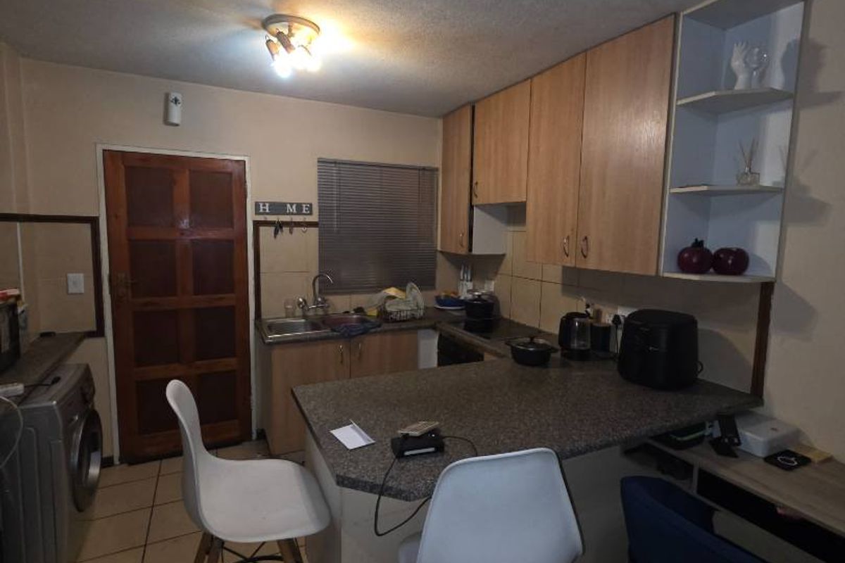 Compact kitchen featuring laminate cabinetry, a breakfast bar, tiled flooring, and a tiled backsplash, offering a functional layout for an apartment setting.