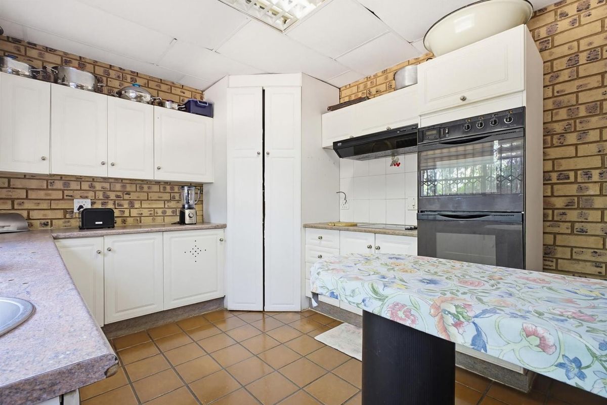 A dated kitchen featuring exposed brick walls, white cabinetry, built-in oven, and drop ceiling tiles, offering potential for a modern renovation.