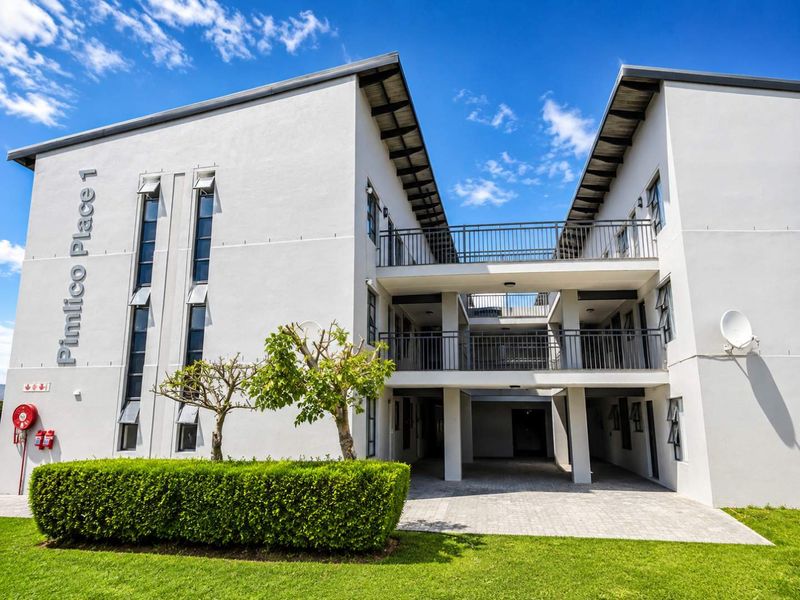 Front elevation of Pimlico Place 1 apartment complex, featuring modern white facade, paved entrance area, and metal balcony railings.