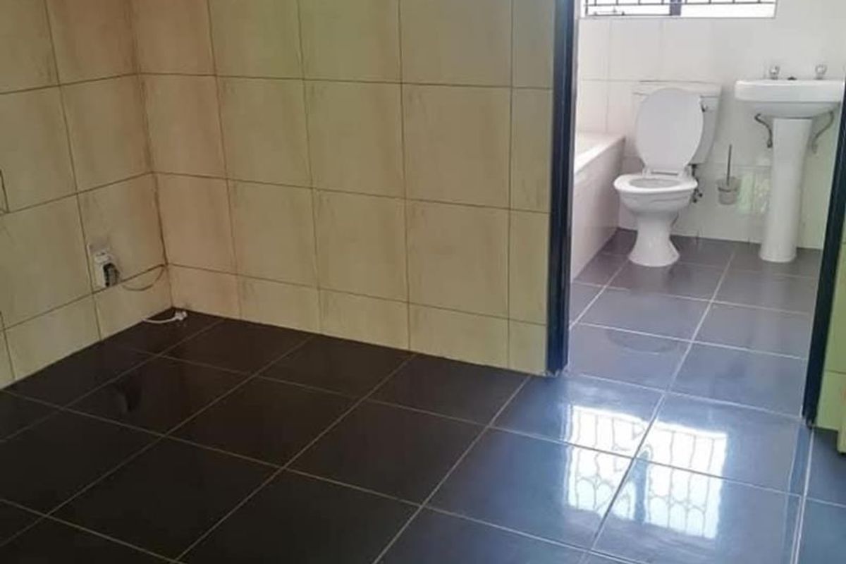 A bathroom featuring a pedestal basin, toilet, and bathtub with dark floor tiles and partially tiled walls showing some damage to the decorative tile border.