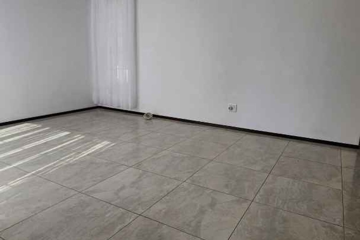 A bright, empty living room featuring neutral floor tiles, white walls, and a simple ceiling light fixture.