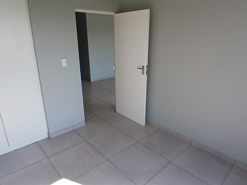 A clean, empty bedroom featuring neutral grey walls, large format floor tiles, and built-in storage cupboards.