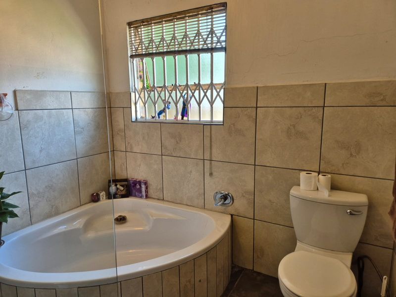 A functional bathroom featuring a corner bathtub, toilet, and tiled wall finishes, complemented by a window with security bars.