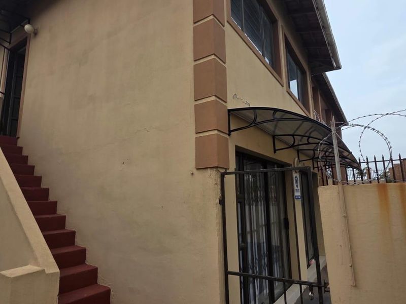Exterior view of the apartment building featuring an external staircase, security gate, and perimeter wall with razor wire fencing.
