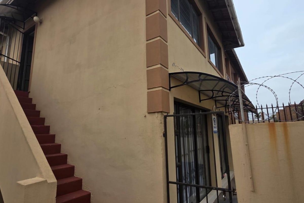Exterior view of the apartment building featuring an external staircase, security gate, and perimeter wall with razor wire fencing.