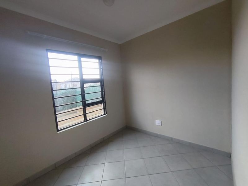 A clean, empty bedroom featuring neutral wall paint, tiled flooring, and a window fitted with security bars.