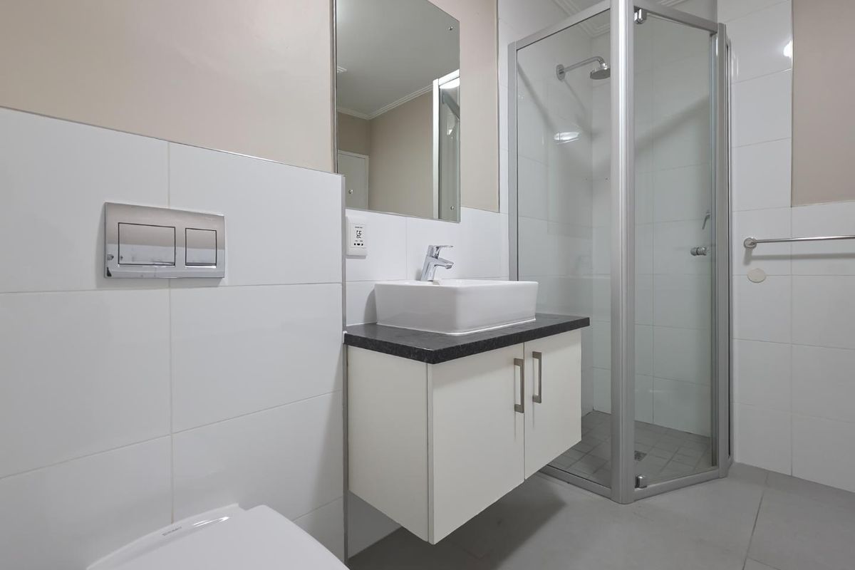 A clean, modern bathroom featuring a wall-mounted toilet, a floating vanity with a vessel sink, and a corner shower enclosure with white wall tiling.