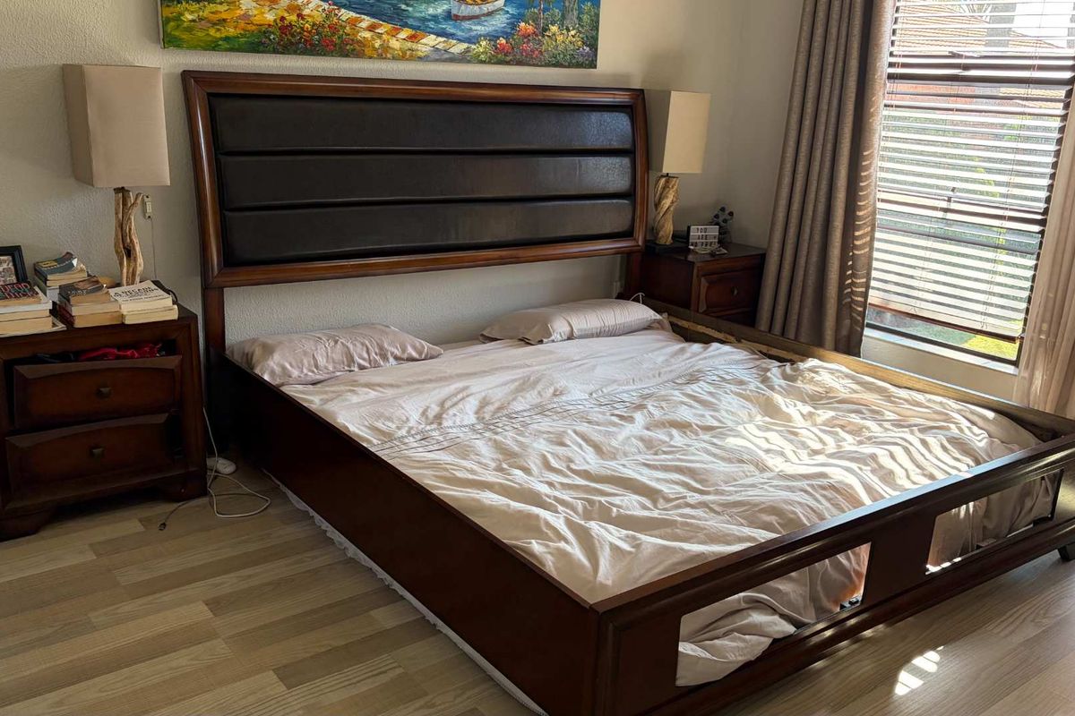 A well-maintained bedroom featuring light-toned laminate flooring and window blinds, providing a neutral foundation for personal styling.