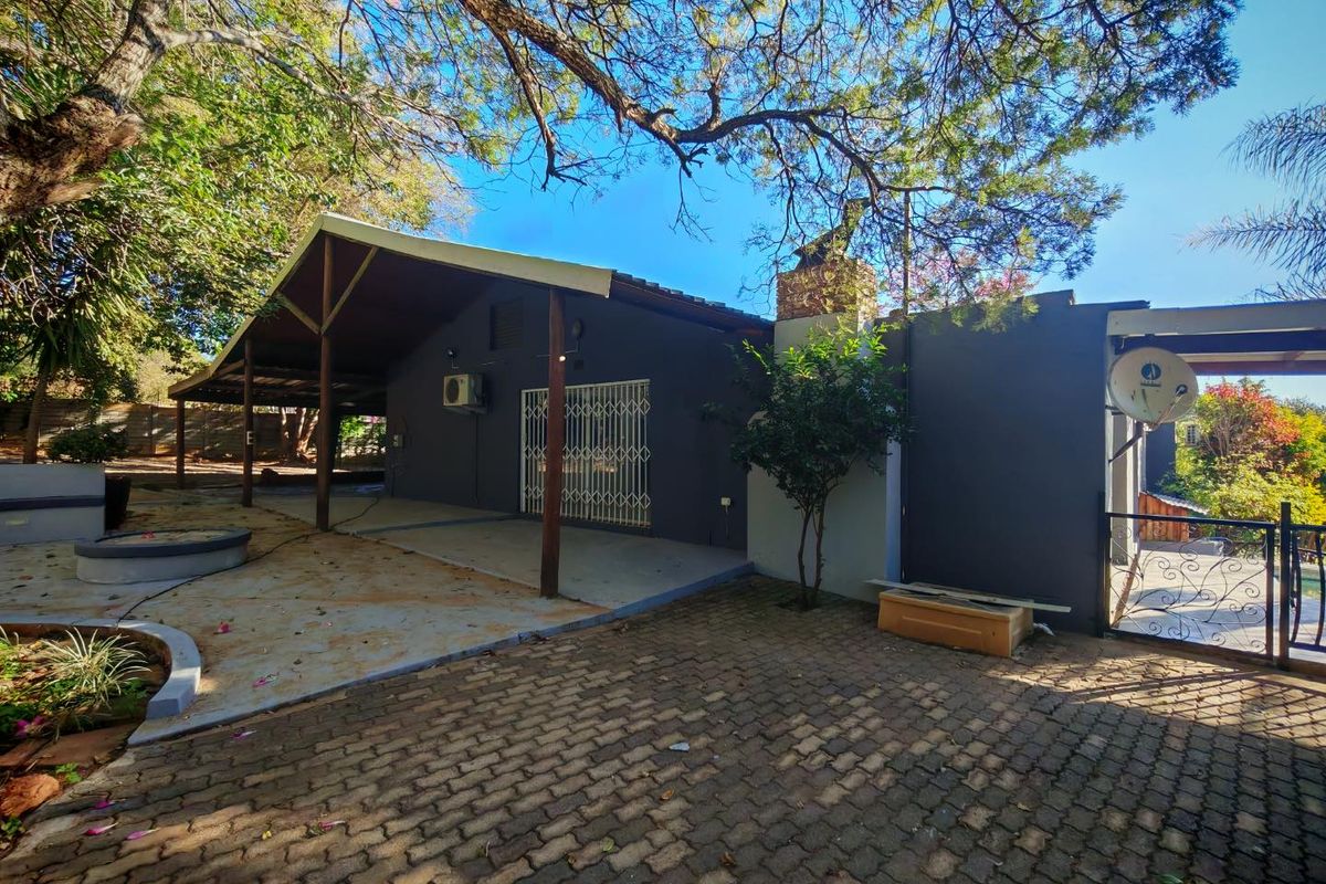 Rear exterior view featuring a covered patio area, paved courtyard, and established trees providing shade.