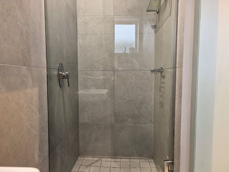 A modern walk-in shower featuring large-format grey marble-look wall tiles, a glass screen, and chrome fixtures.