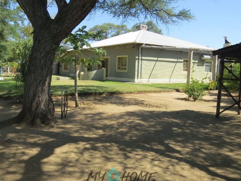 A view of the rear exterior of the house, featuring a metal roof, security bars on windows, and a spacious garden area.