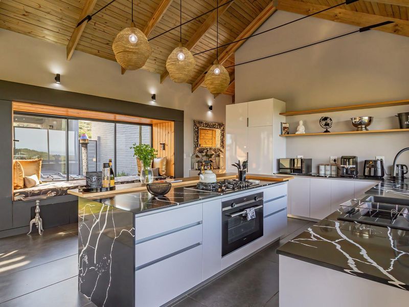 Modern kitchen featuring a large island with stone countertops, built-in appliances, vaulted timber ceilings, and a cozy integrated window seat.