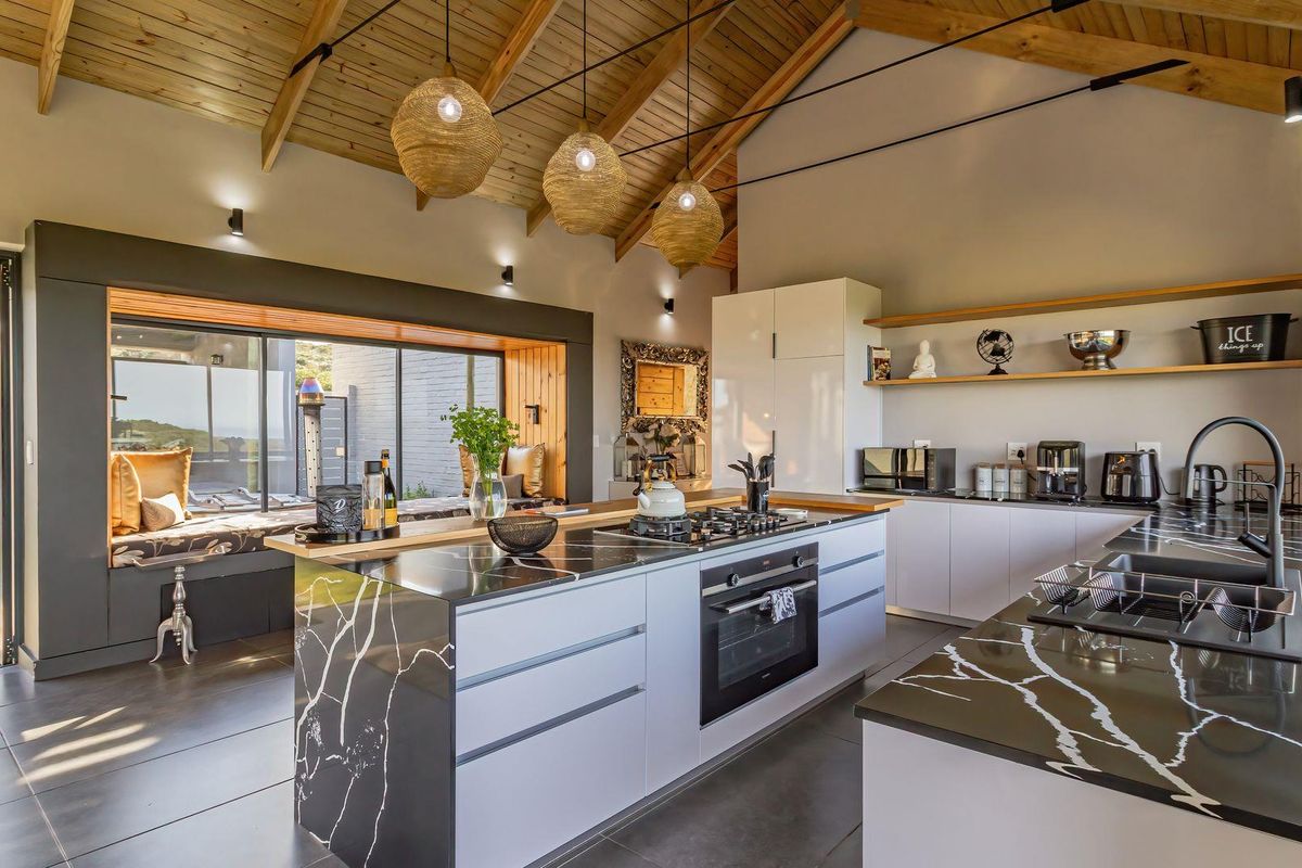 Modern kitchen featuring a large island with stone countertops, built-in appliances, vaulted timber ceilings, and a cozy integrated window seat.