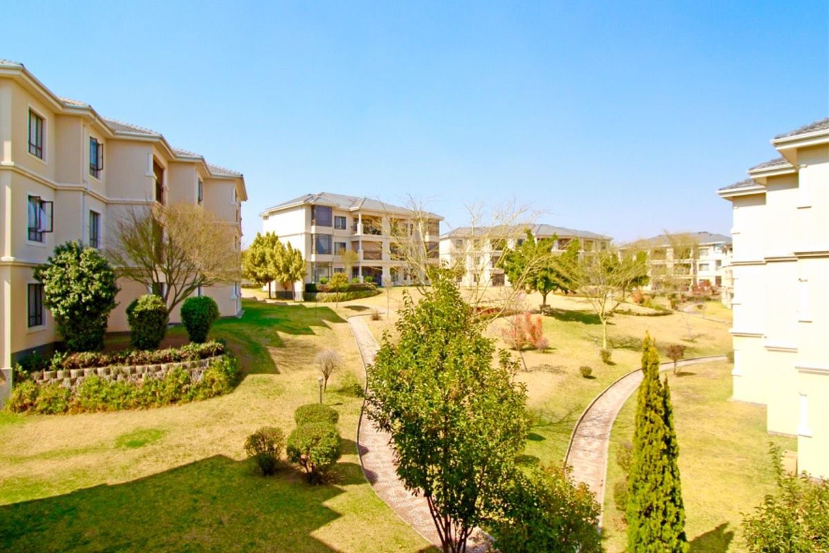 A view of the well-maintained communal gardens and paved pathways situated between the apartment complex buildings.