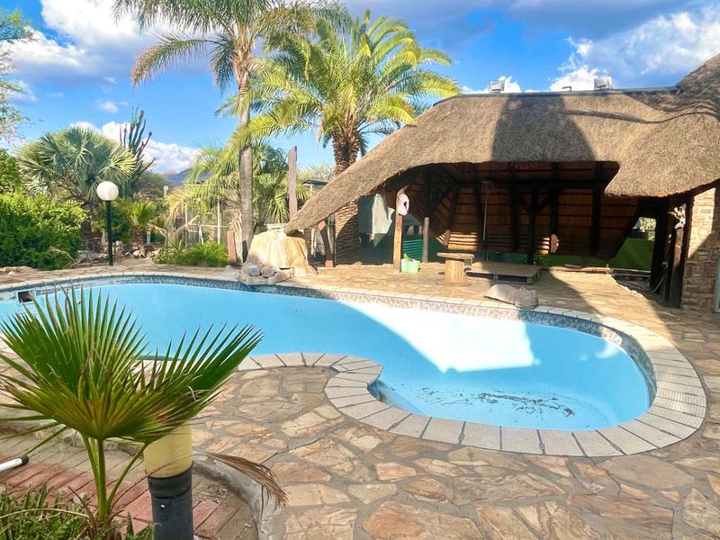 Outdoor pool area featuring a swimming pool, stone paving, and a traditional thatched lapa, ideal for relaxation and entertainment.