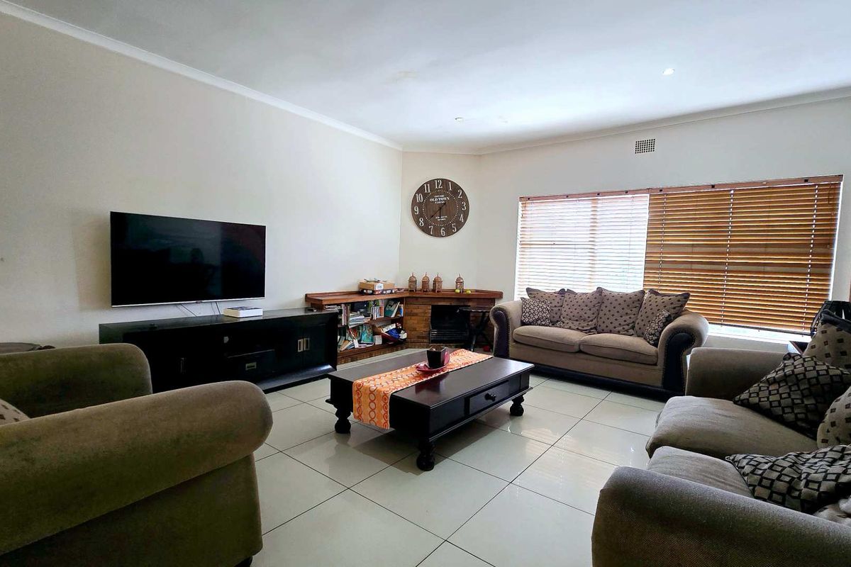 A spacious living room featuring large format floor tiles, recessed downlighting, and wooden window blinds.