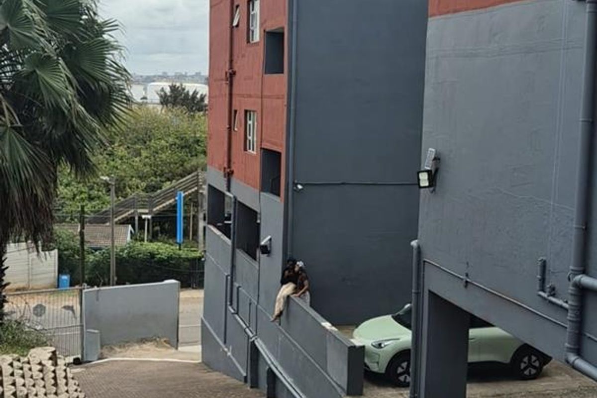 Exterior view of the apartment building complex featuring a paved driveway, retaining wall, and multi-story facade with security lighting.
