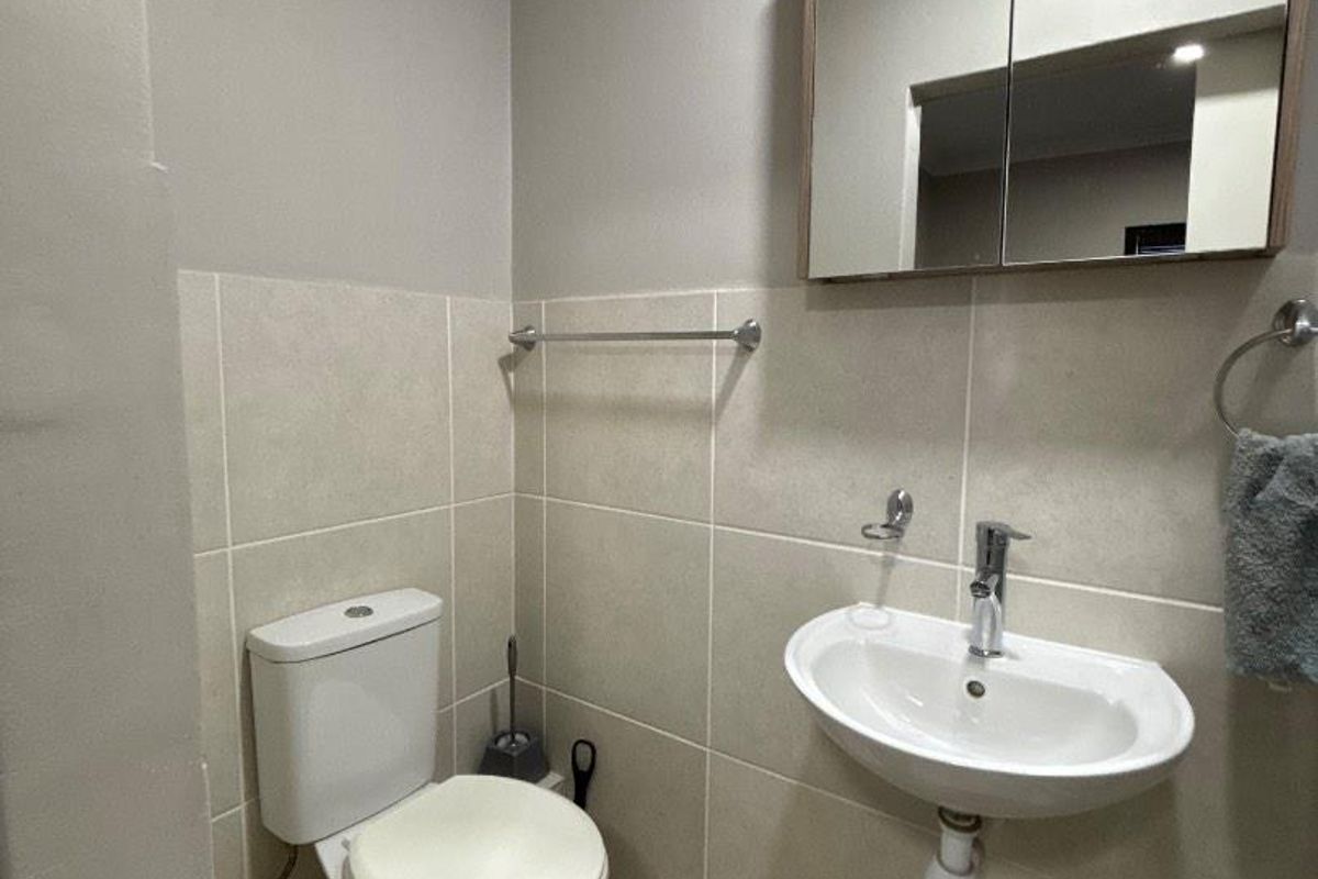 A compact, well-maintained bathroom featuring a wall-mounted basin, toilet, and mirrored medicine cabinet with neutral wall and floor tiling.