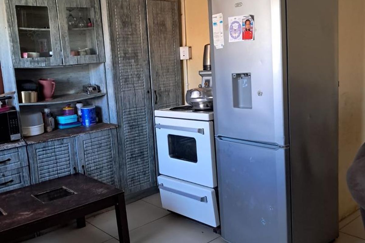 A functional kitchen area featuring tiled flooring, built-in cabinetry, and a freestanding stove, requiring cosmetic updates to improve the overall aesthetic.