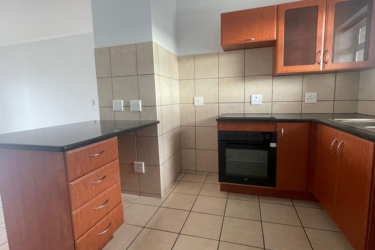 A functional kitchen featuring wooden cabinetry, granite countertops, a built-in oven with hob, and neutral ceramic tile flooring and backsplash.
