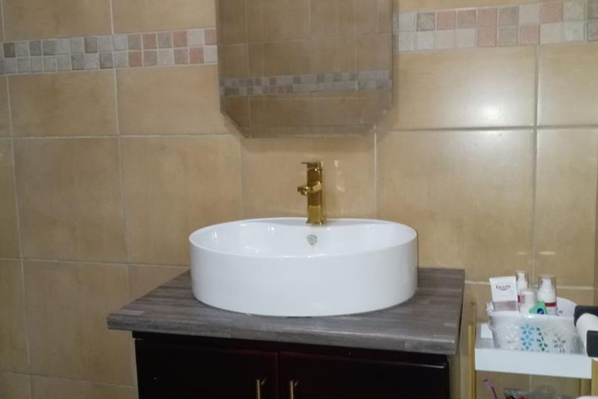 A bathroom vanity area featuring a white vessel sink, gold-tone faucet, dark wood-finish cabinet, and neutral ceramic wall tiling.